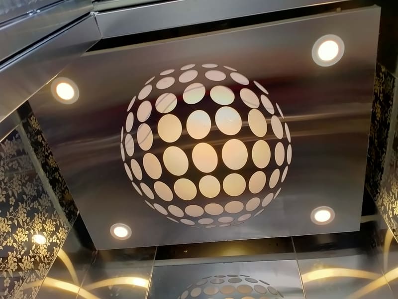 Lift cabin ceiling with a spherical perforated light feature and spotlights